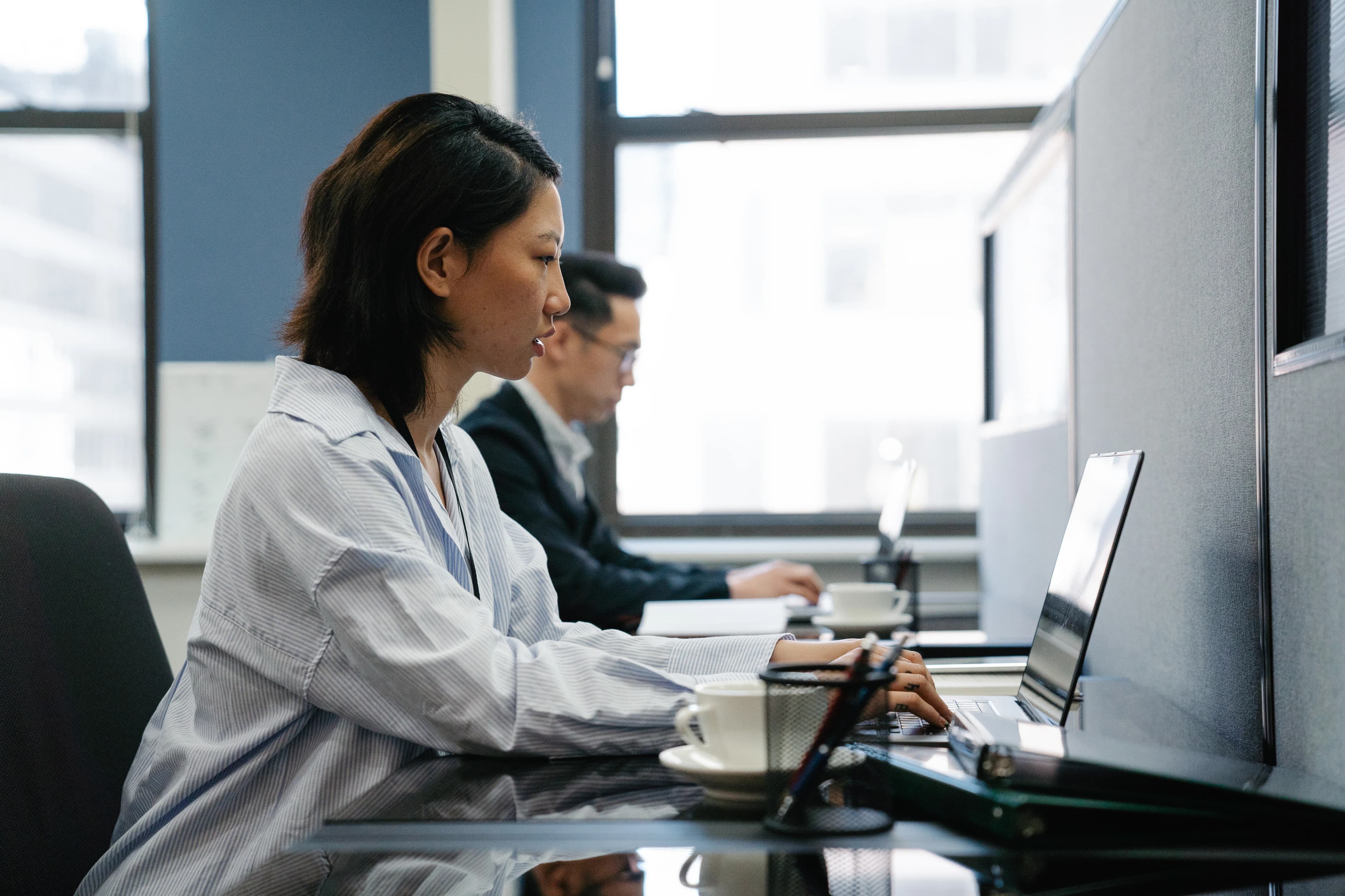 Two professionals working on laptops in a modern office.
